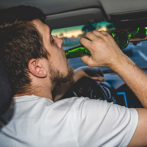 Man drinking beer while driving, illustrating the impact of a DUI conviction in California.